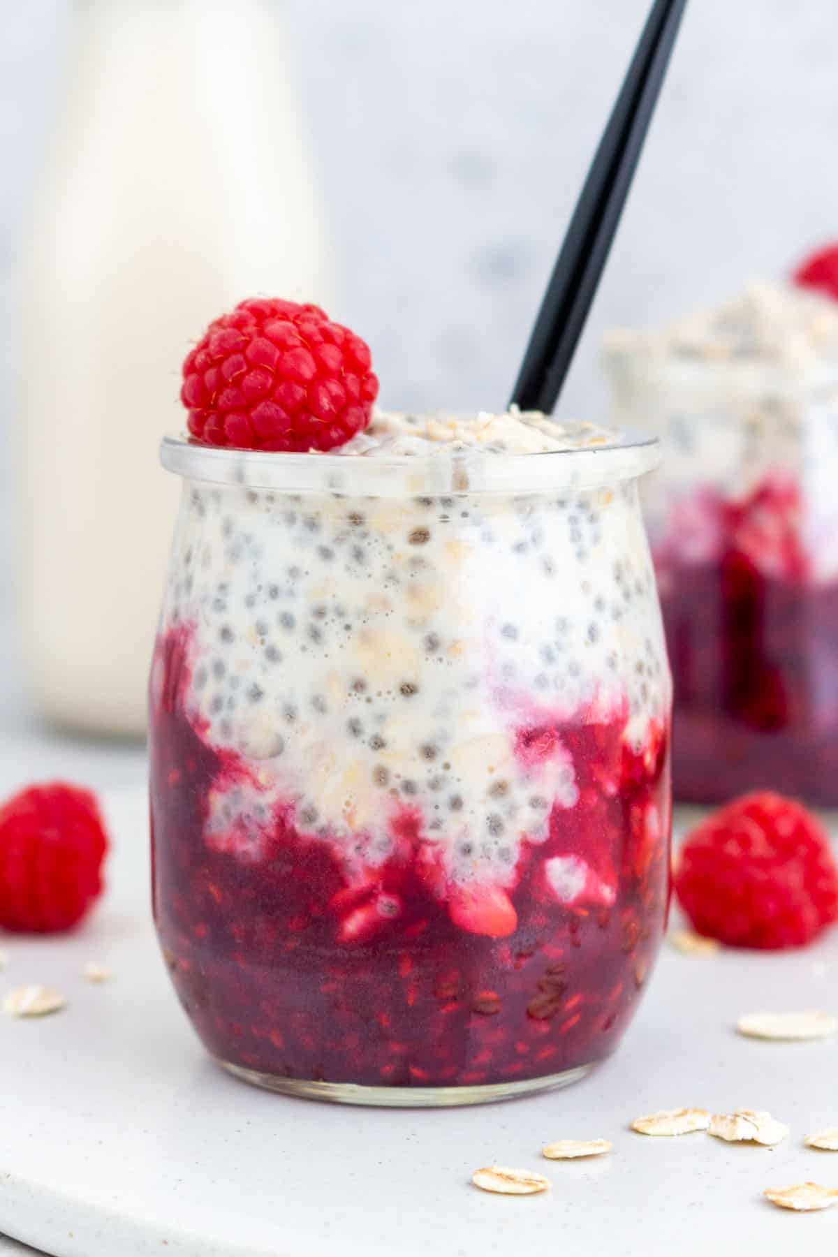 A jar of raspberry overnight oats with a fresh raspberry on top with a spoon inside.