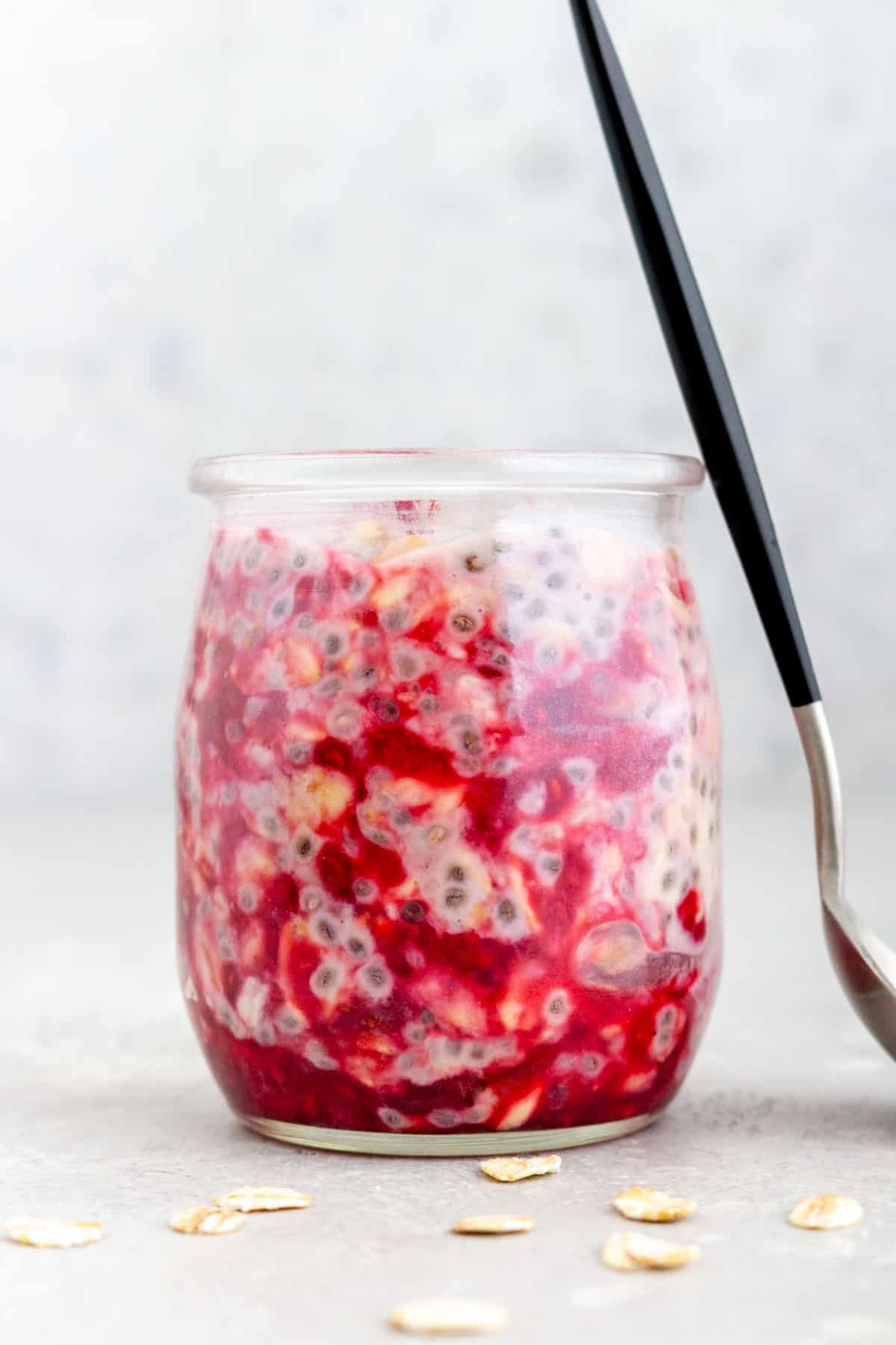 A jar of raspberry overnight oats with a spoon leaning against it.