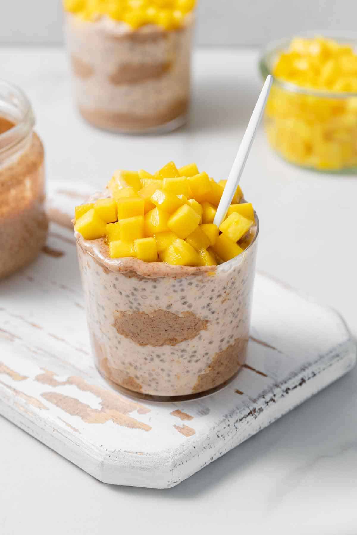 A jar of almond butter overnight oats with diced mango on top with a spoon inside.