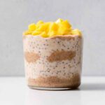A glass of almond butter overnight oats with diced mango on top.