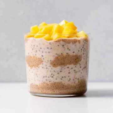 A glass of almond butter overnight oats with diced mango on top.