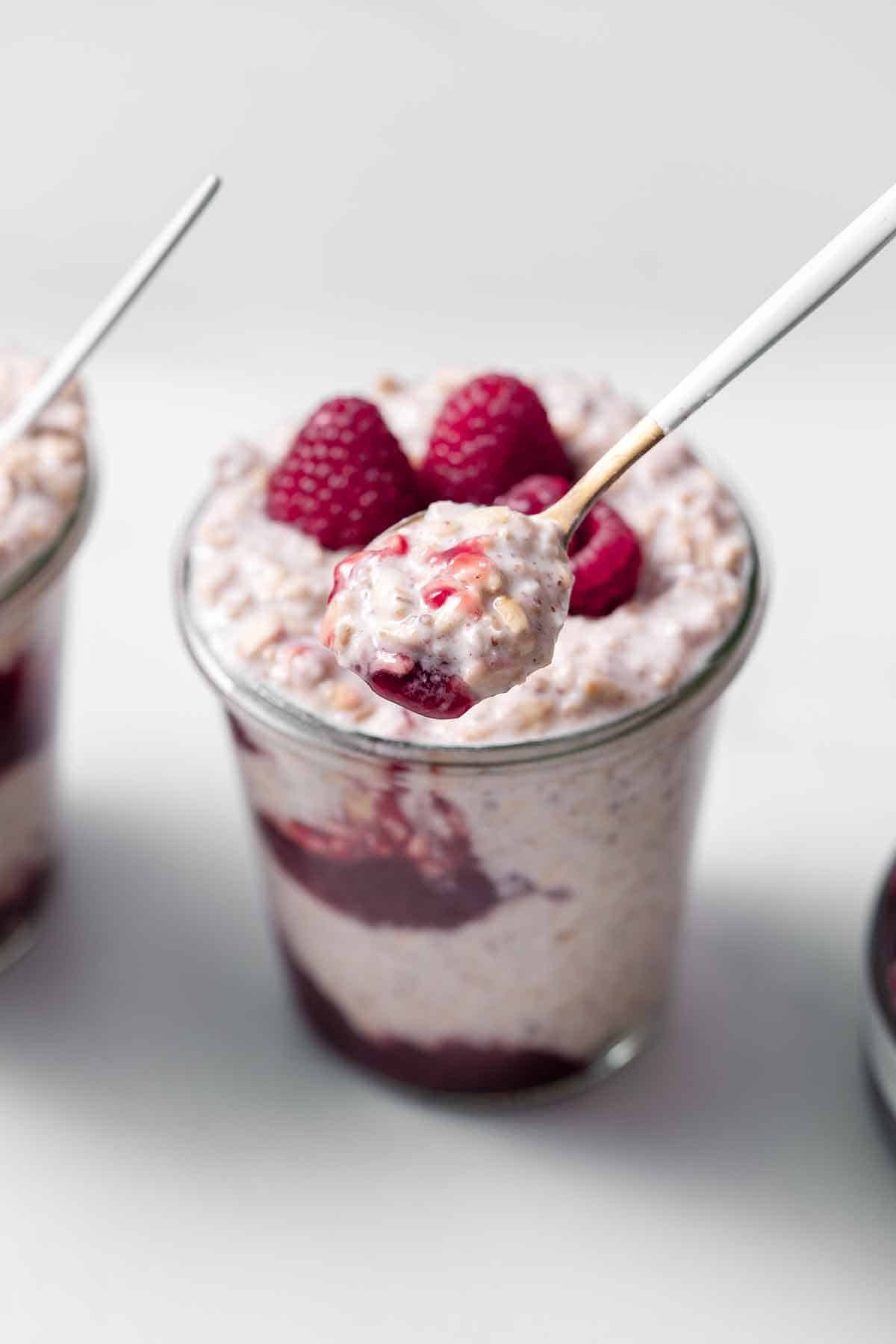 A spoonful of overnight oats without chia seeds in front of a jar of overnight oats topped with raspberries.