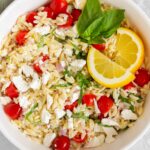 Overhead view of a bowl of lemon orzo salad with feta with basil and sliced lemons.