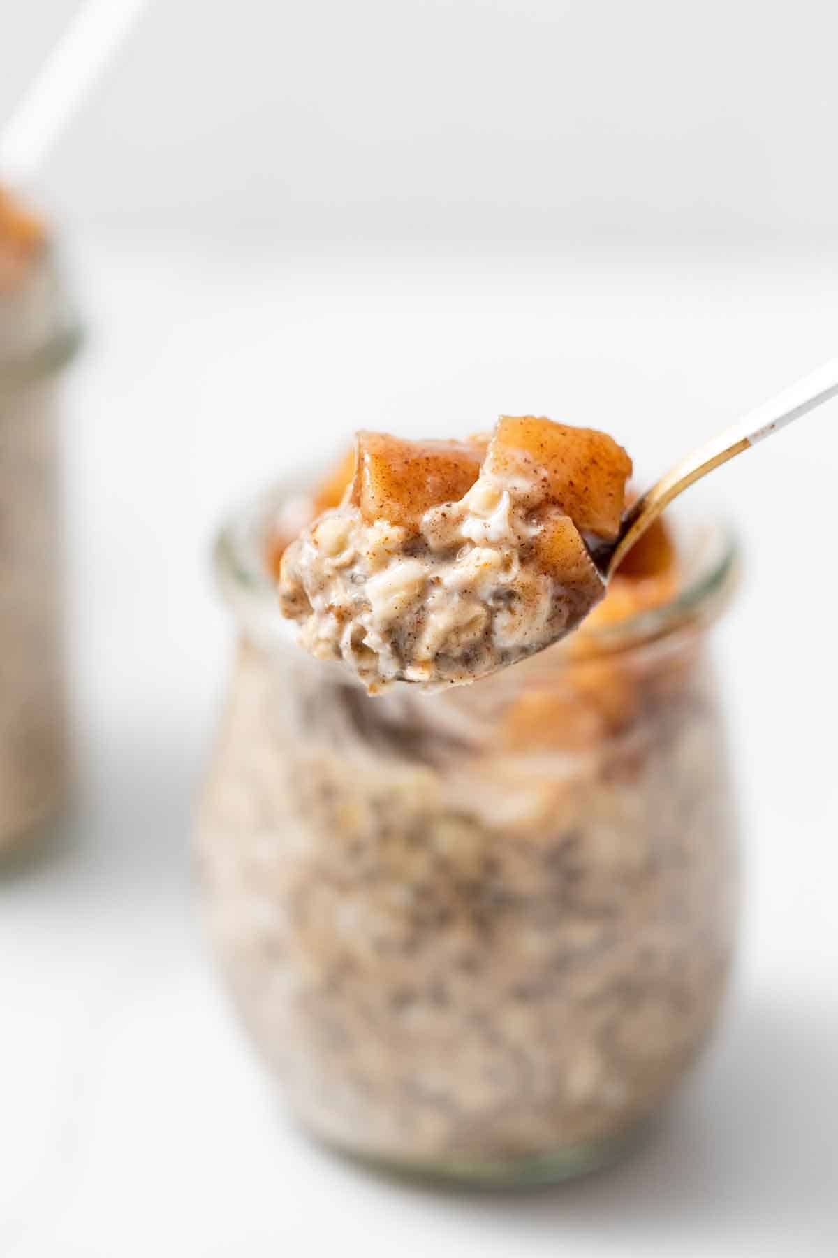 A spoonful of apple cinnamon overnight oats in front of a jar.