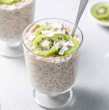 A glass of coconut overnight oats topped with shredded coconut and kiwi.