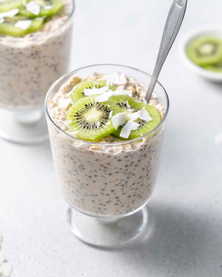 A glass of coconut overnight oats topped with shredded coconut and kiwi.