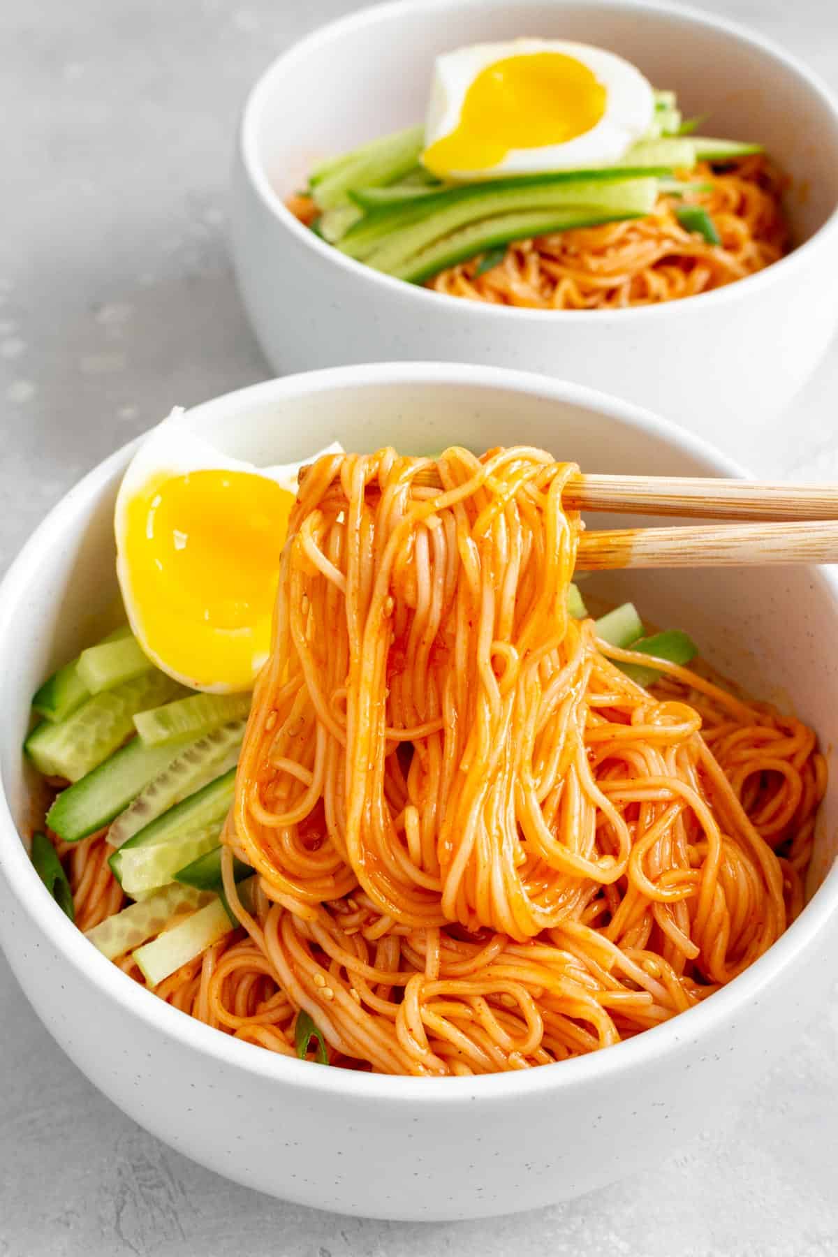 A bowl of bibim guksu with a pair of chopsticks lifting up some noodles.