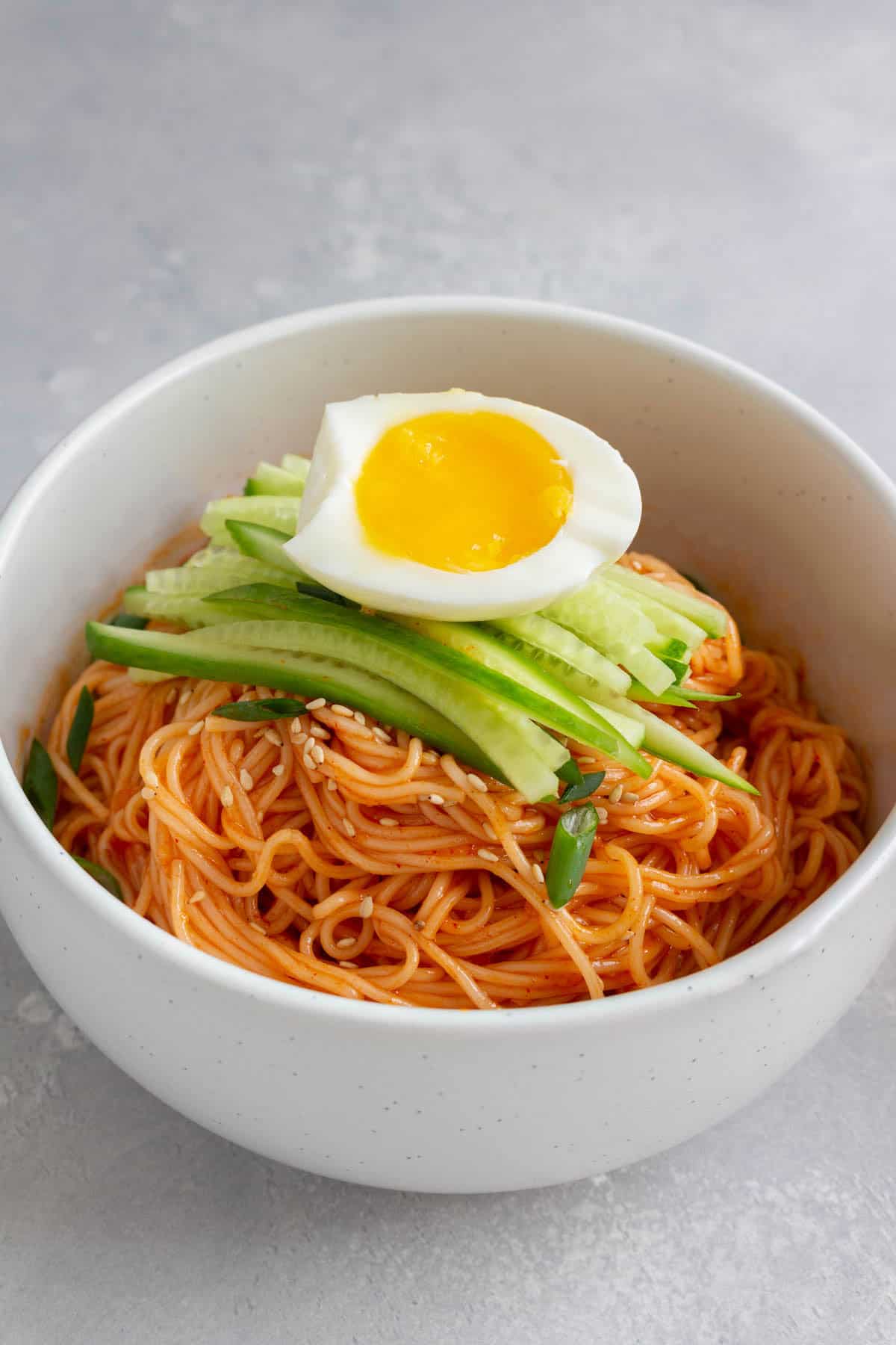 A bowl of bibim guksu with sliced cucumbers and half an egg on top.
