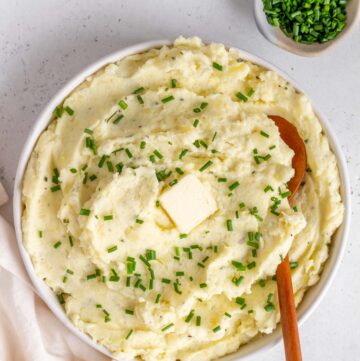 Overhead view of a bowl of Boursin mashed potatoes topped with chives and butter.