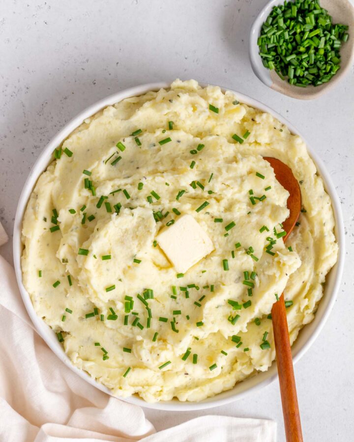 Overhead view of a bowl of Boursin mashed potatoes topped with chives and butter.