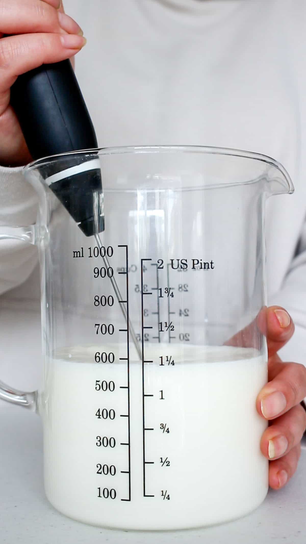 A handheld frother in a measuring cup of dairy.