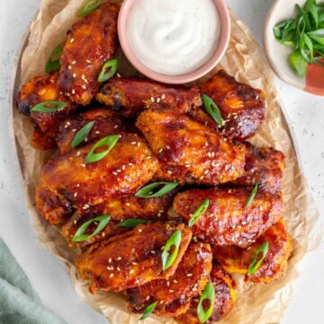 Overhead view of a platter lined with parchment paper full of crispy bbq chicken wings with a small bowl of dip.