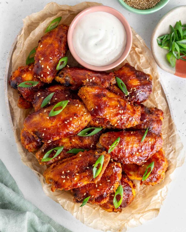 Overhead view of a platter lined with parchment paper full of crispy bbq chicken wings with a small bowl of dip.