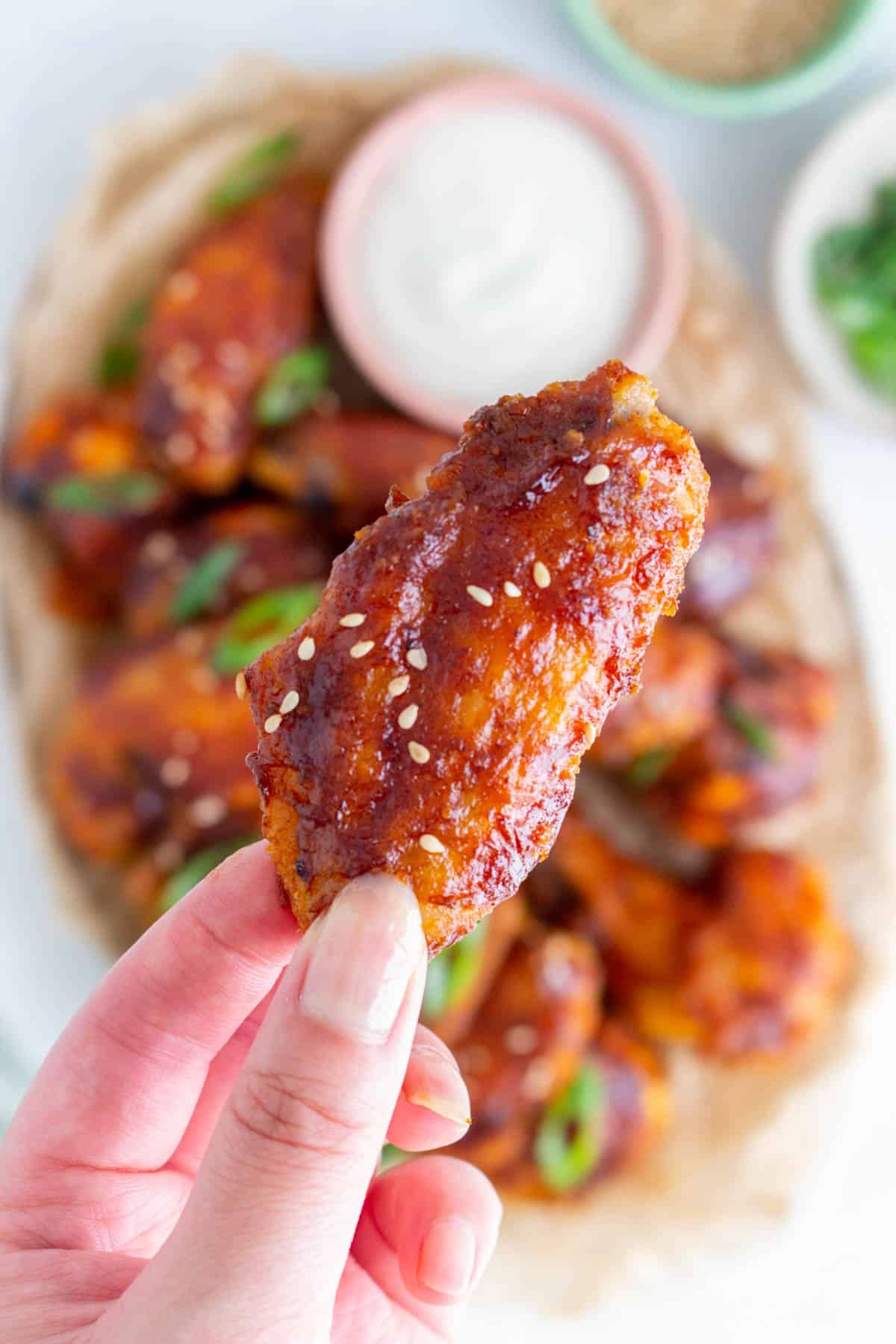 A hand holding up a crispy bbq chicken wing with some sesame seeds.