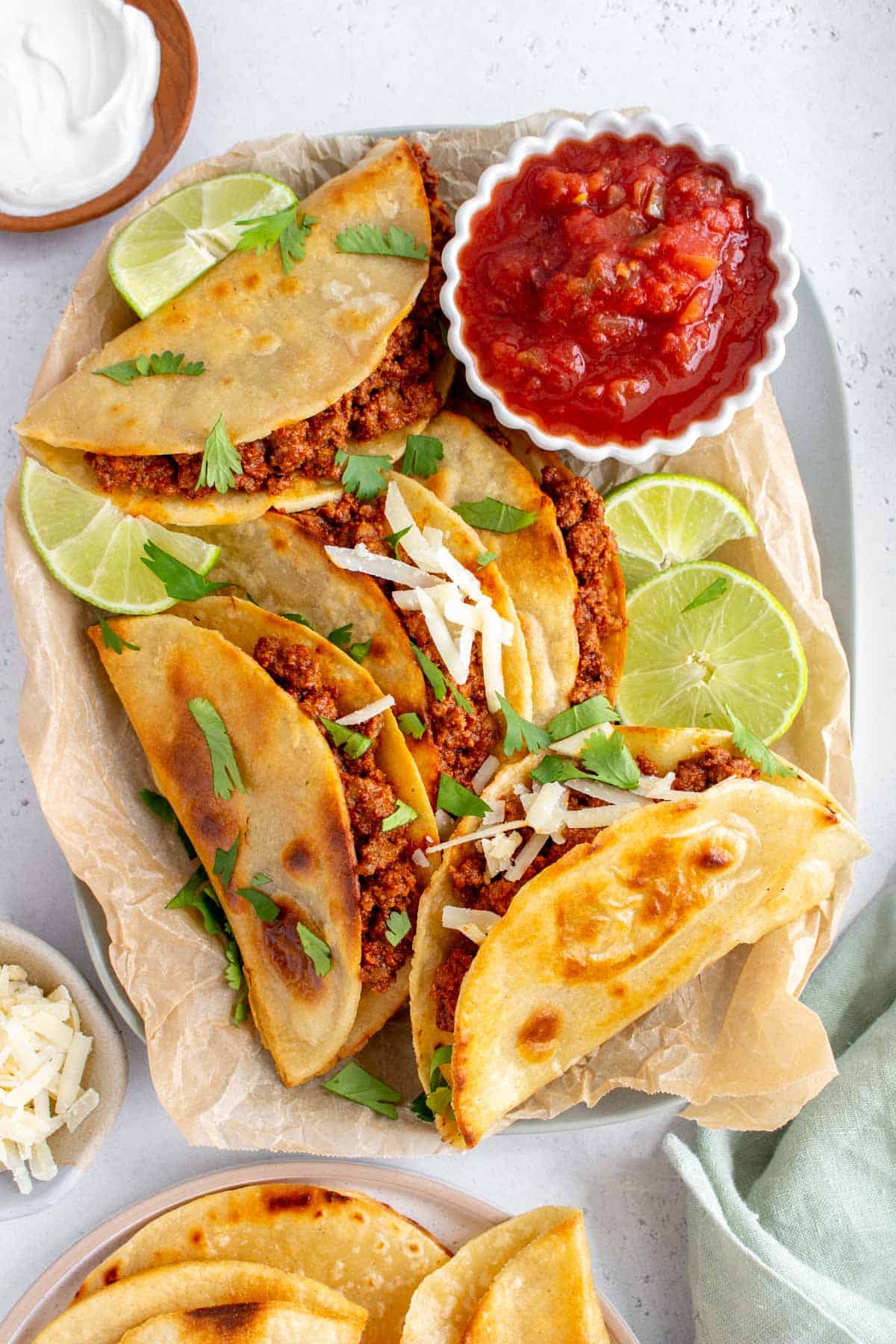 A platter of beef tacos with cilantro and shredded cheese scattered on top.