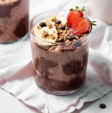 A jar of nutella overnight oats with cut strawberries, bananas, chocolate chips, and granola.