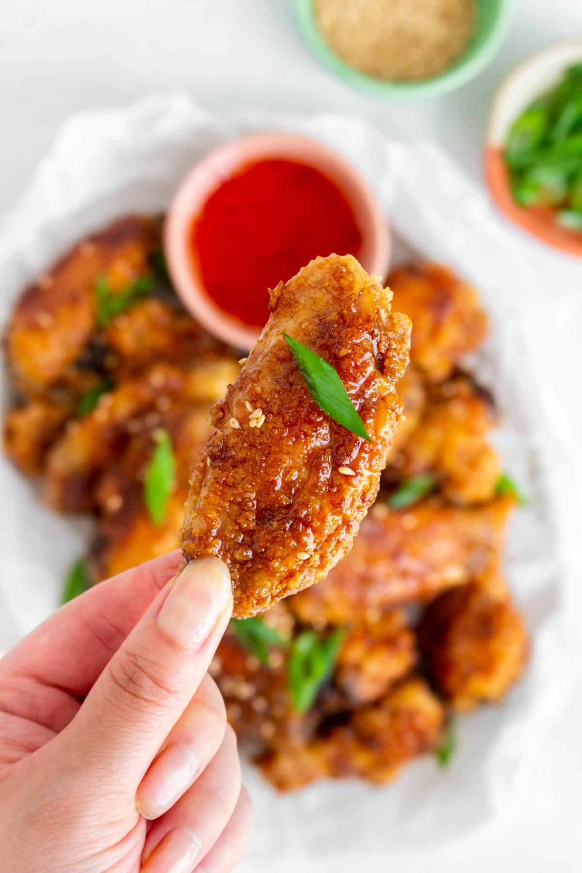 A hand holding up a soy garlic chicken wing.