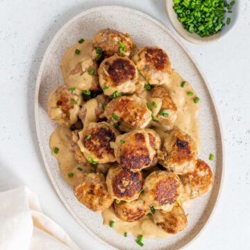 Overhead view of an oval platter of turkey Swedish meatballs with gravy and chives.