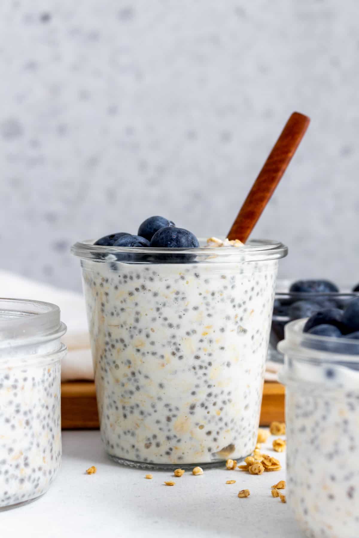 A jar of vanilla overnight oats with blueberries on top and a spoon inserted.