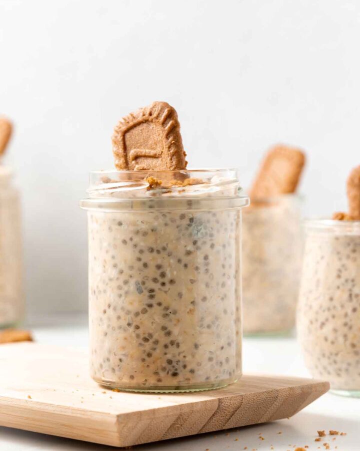 A jar of biscoff overnight oats with a cookie stuck in with more in the background.