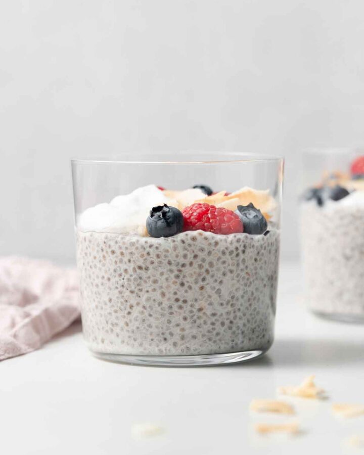 Profile view of a glass of coconut cream chia pudding with some berries and cream on top.