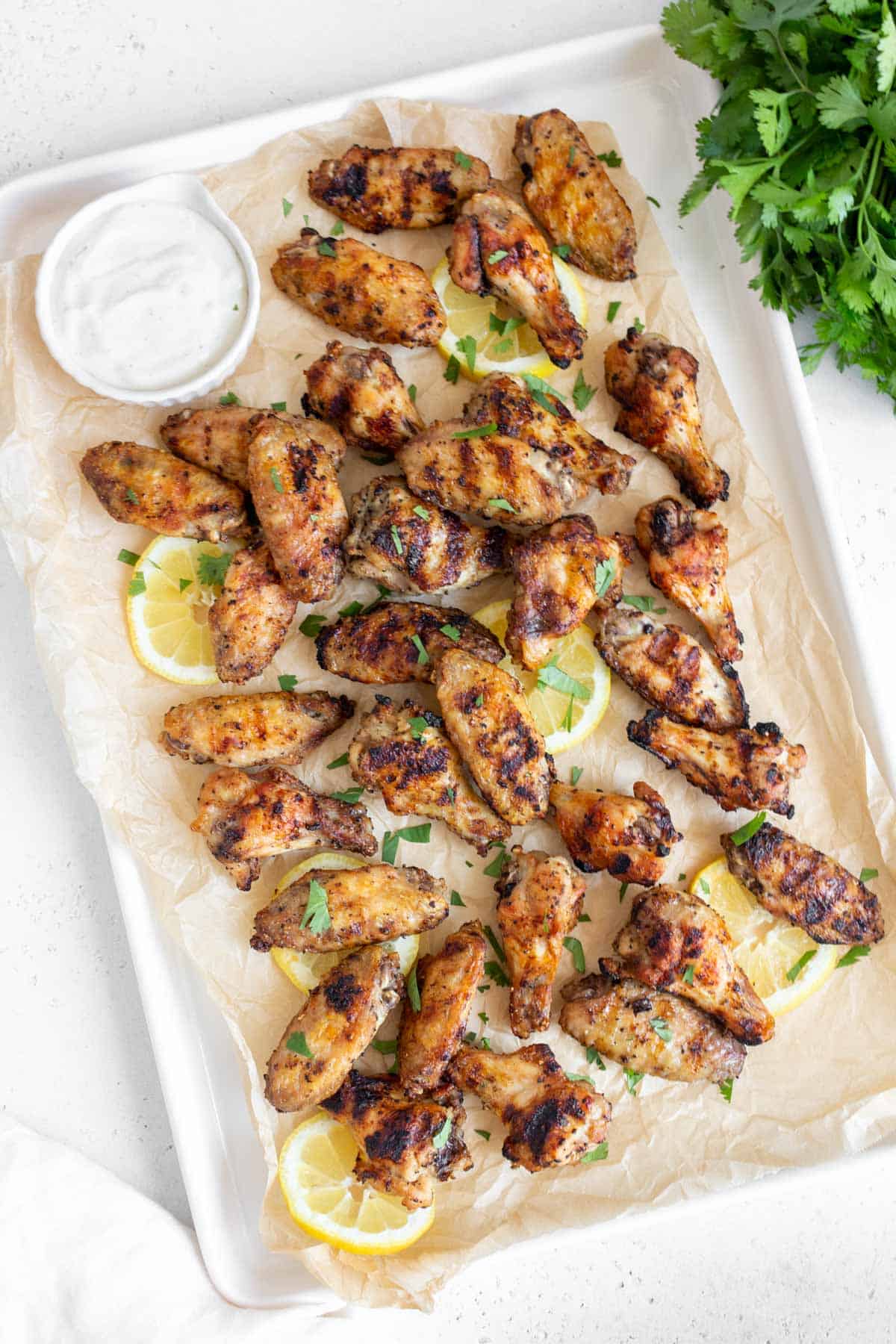 Overhead view of grilled chicken wings on a sheet pan with cilantro and lemon slices as garnish.