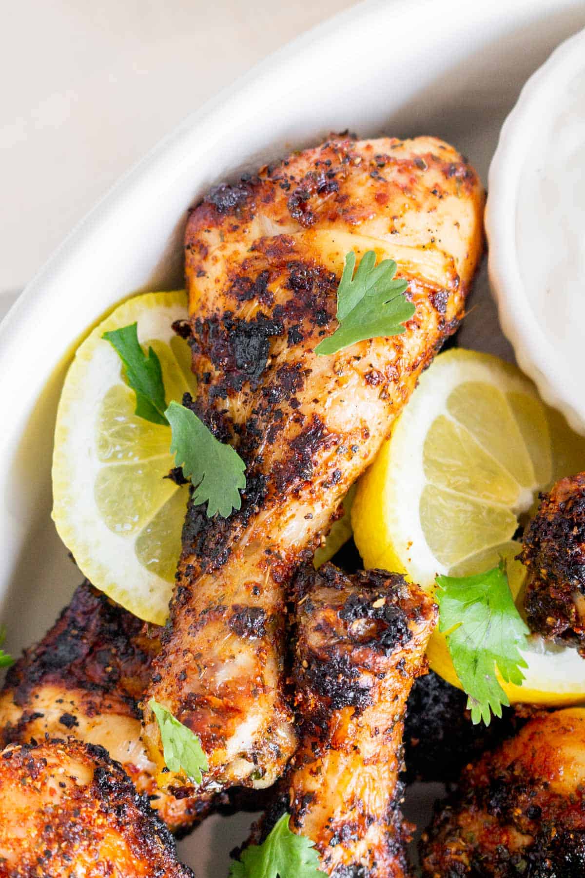 Close up view of a grilled chicken drumstick with cilantro surrounded by lemon slices.