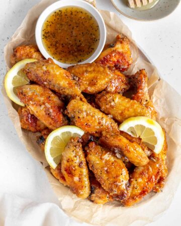 Overhead view of a platter of honey lemon pepper wings with lemon slices and a bowl of sauce.