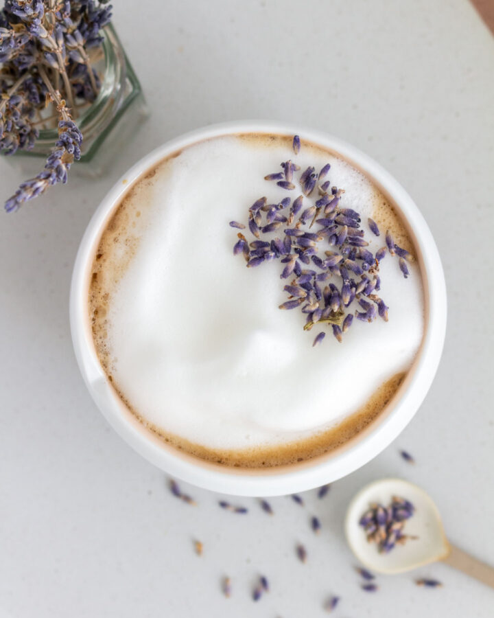 Overhead view of a lavender latte in a mug with foam on top, garnished with lavender buds.