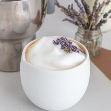 A lavender latte with some lavender in the background.