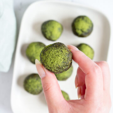 A hand holding a matcha ball above a plate with more energy balls.