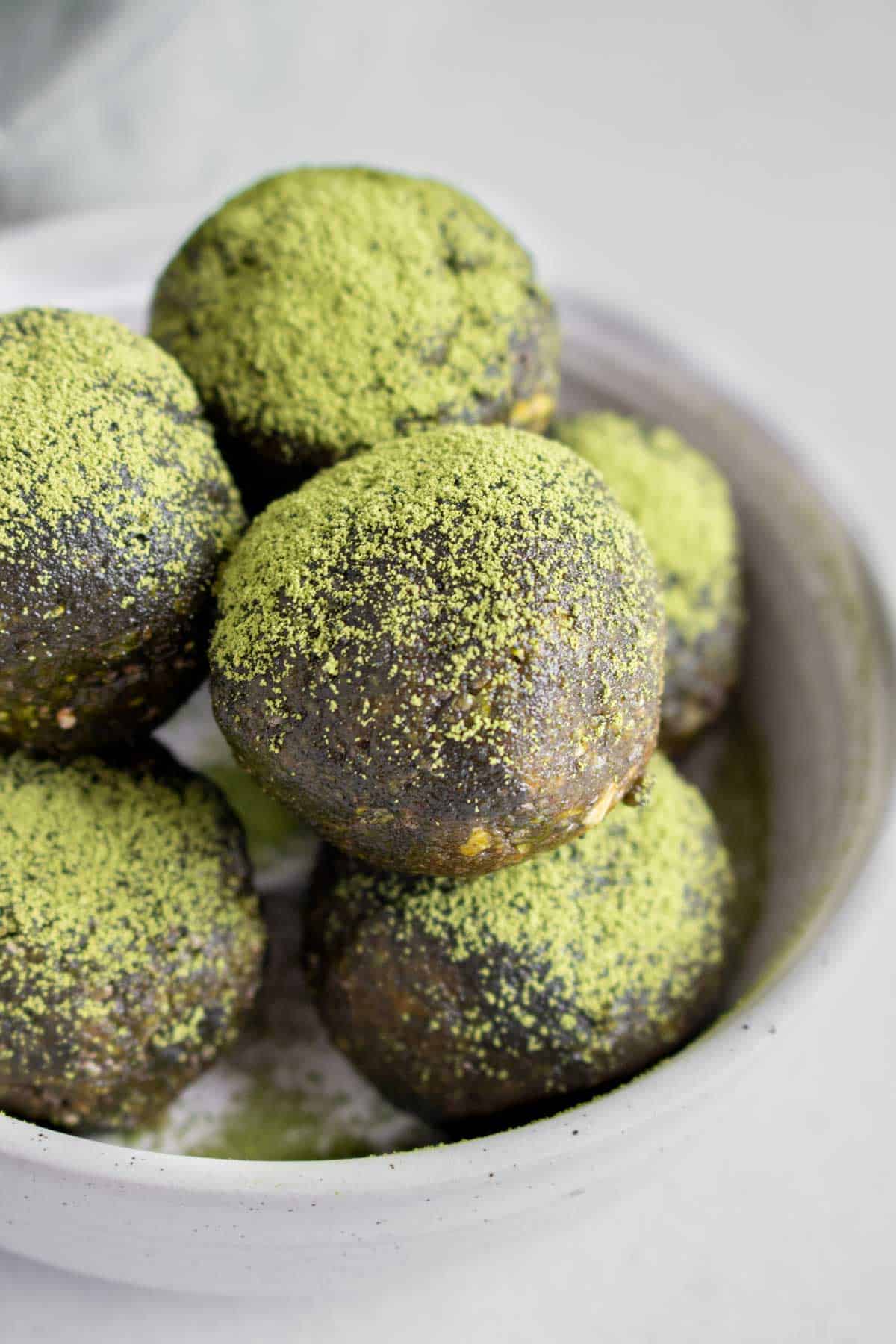 Close up view of matcha energy balls stacked in a bowl with a dusting of matcha powder on top.