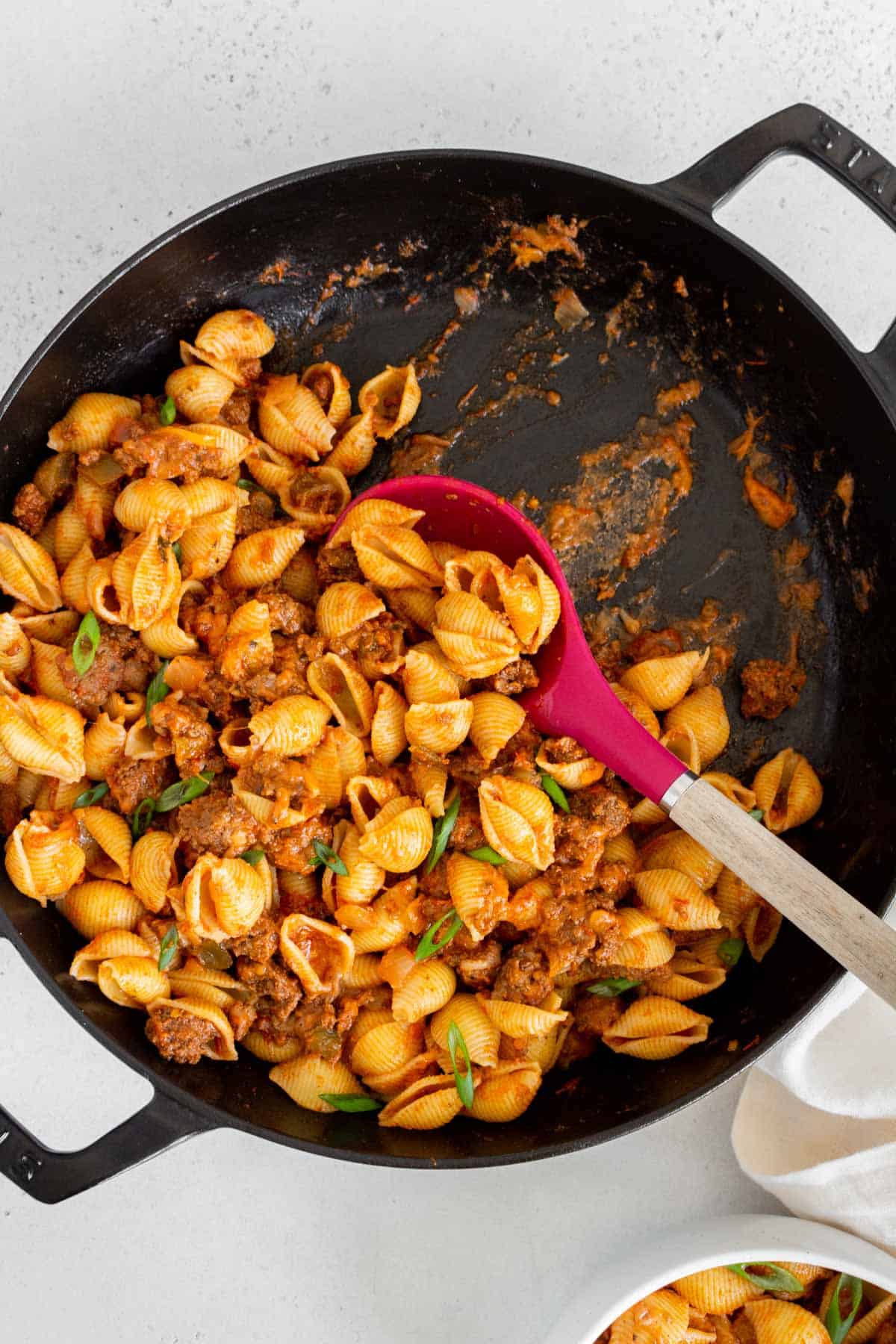 A skillet of taco pasta half scooped out. Spoon i the skillet.