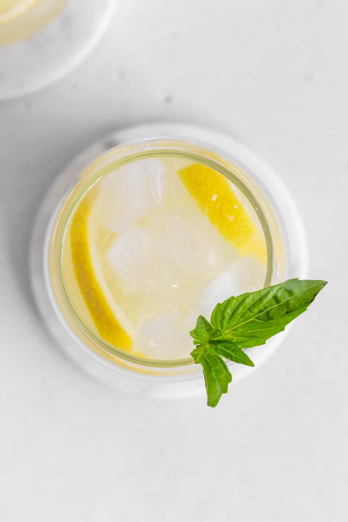 Overhead view of a glass of basil lemonade with ice and basil garnish on top.