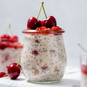Profile view of a jar of cherry overnight oats with fresh cherries on top.
