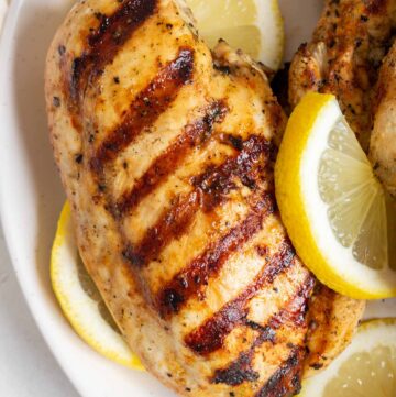 Overhead view of a grilled lemon pepper chicken with grill marks with sliced lemons around it.
