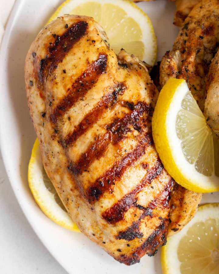 Overhead view of a grilled lemon pepper chicken with grill marks with sliced lemons around it.