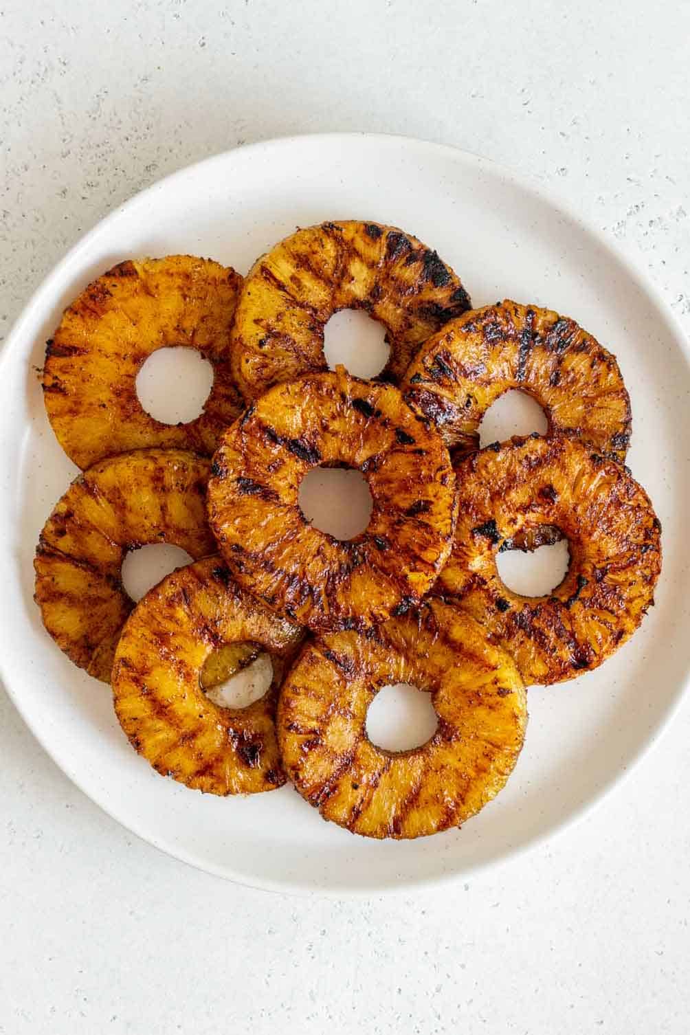 Overhead view of a plate with multiple grilled pineapple rings.