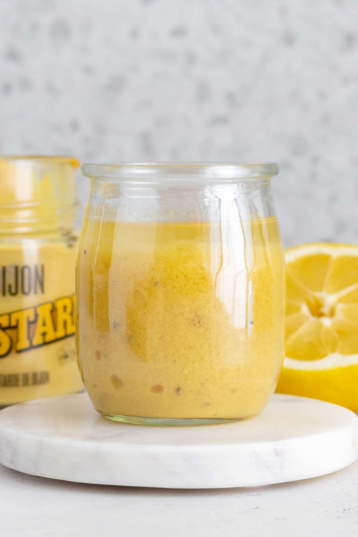 A jar of lemon honey dijon vinaigrette on a marble coaster.
