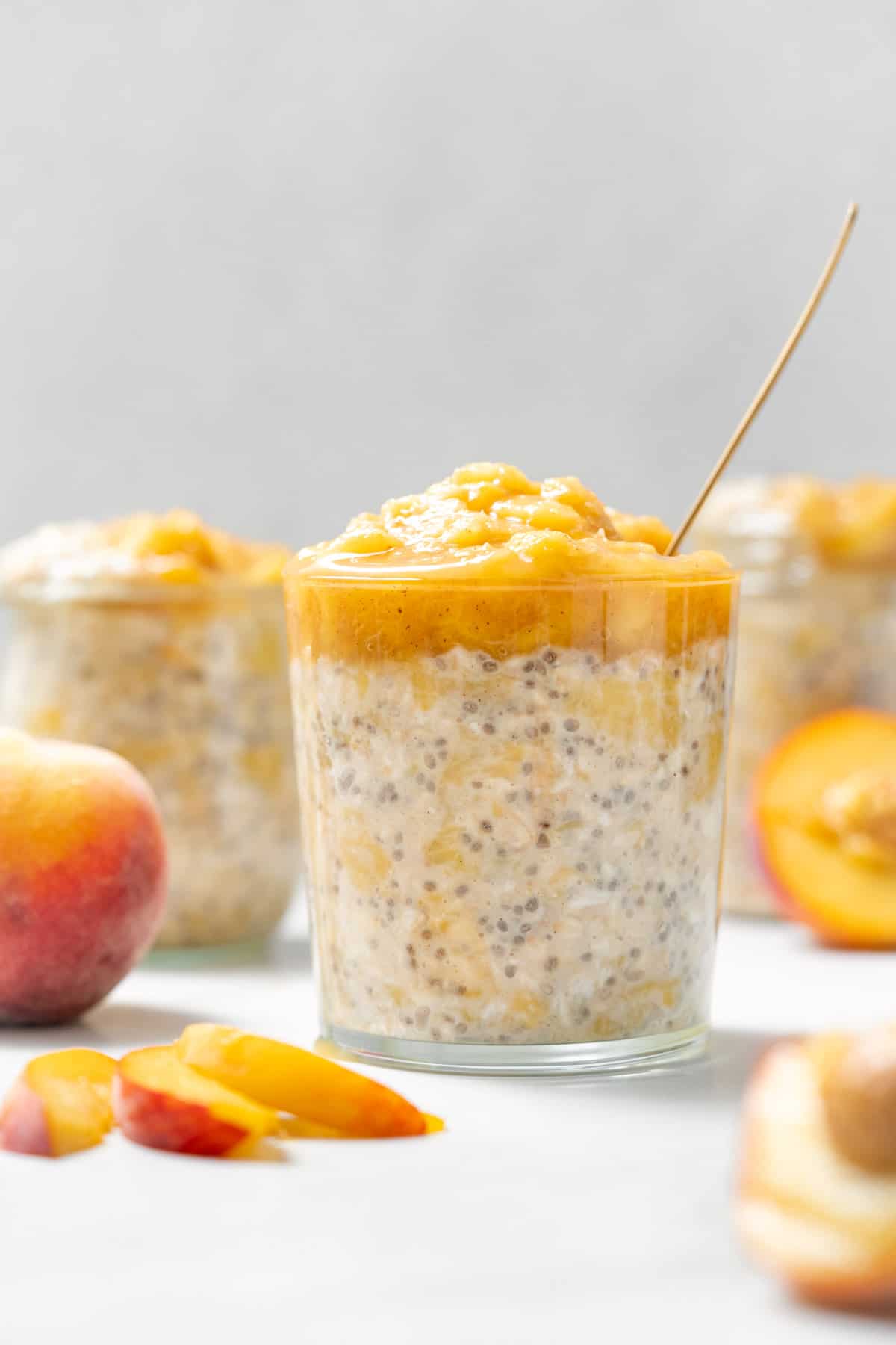 A glass with peach overnight oats topped with cooked peaches with cut peaches around it.