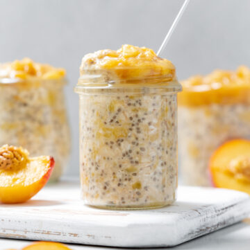A jar of peach overnight oats on a serving board with cut peaches around it.
