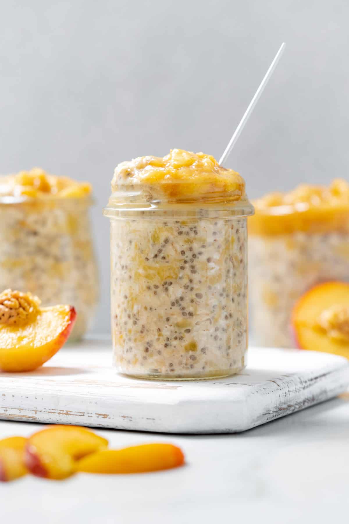 A jar of peach overnight oats on a serving board with cut peaches around it.