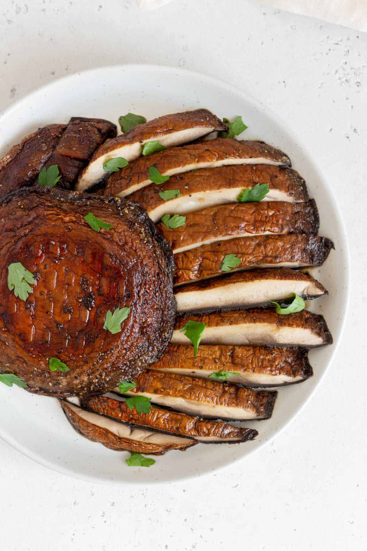 Overhead view of a plate with sliced air fryer portobello mushrooms on a plate with one full mushroom.