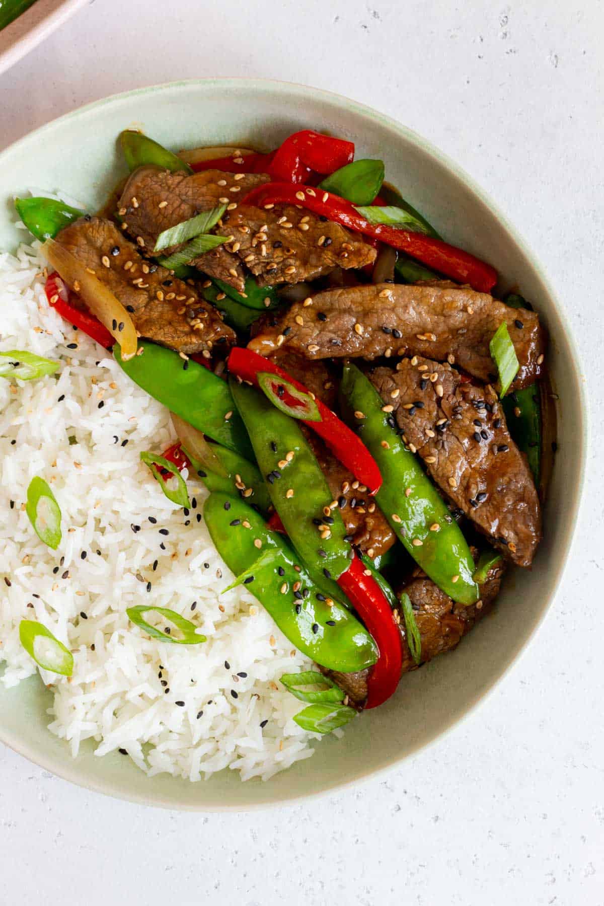Overhead view of a bowl of rice with beef with oyster sauce and green onions.