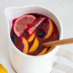 An angled view of a pitcher of blueberry lemonade with a wooden spoon inside.