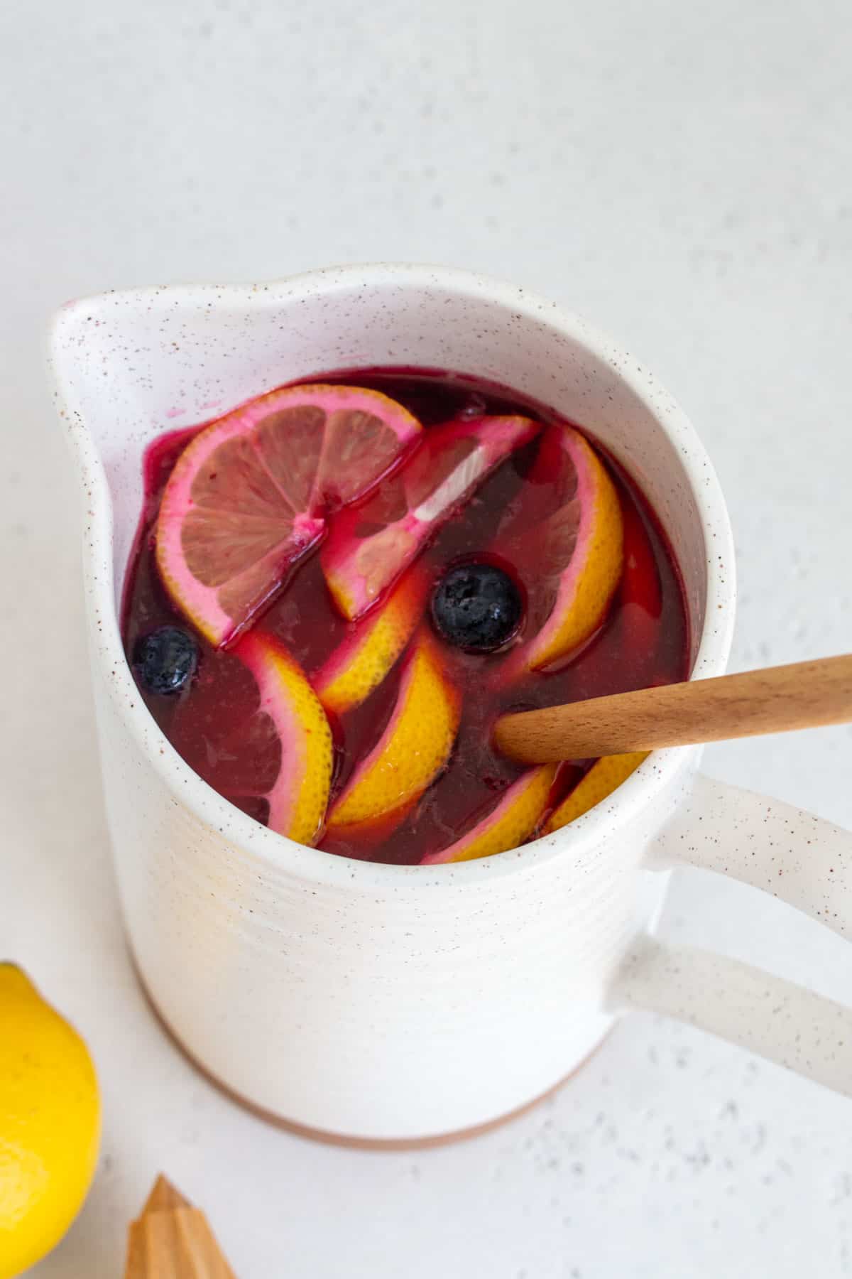 An angled view of a pitcher of blueberry lemonade with a wooden spoon inside.