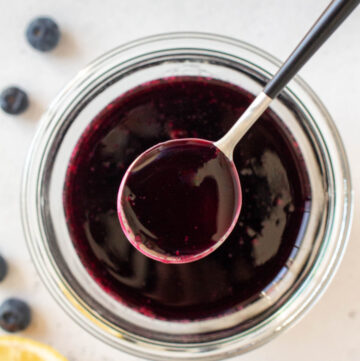 Overhead view of a spoonful of blueberry simple syrup lifted from a jar.