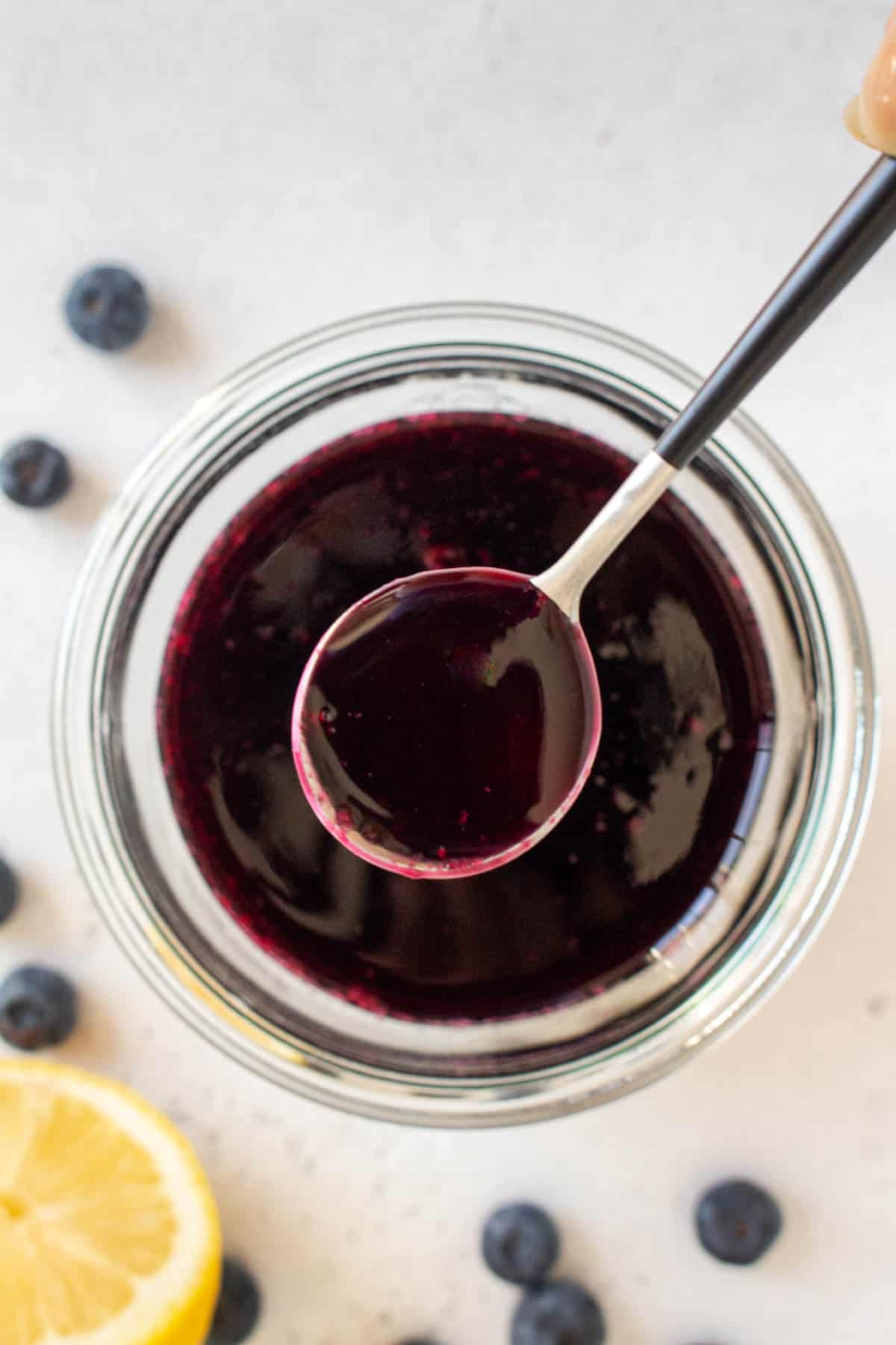 Overhead view of a spoonful of blueberry simple syrup lifted from a jar.