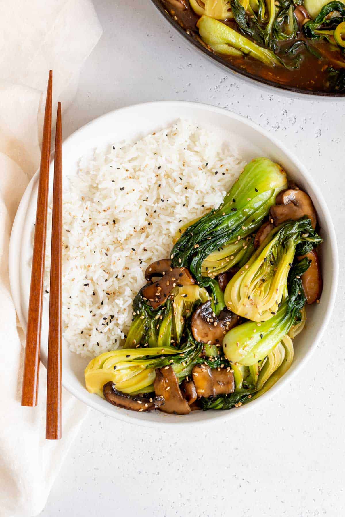 A plate of rice and bok choy stir fry with a pair of chopsticks on the side.
