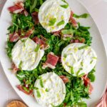 Overhead view of a platter with arugula, prosciutto, burrata, and basil.